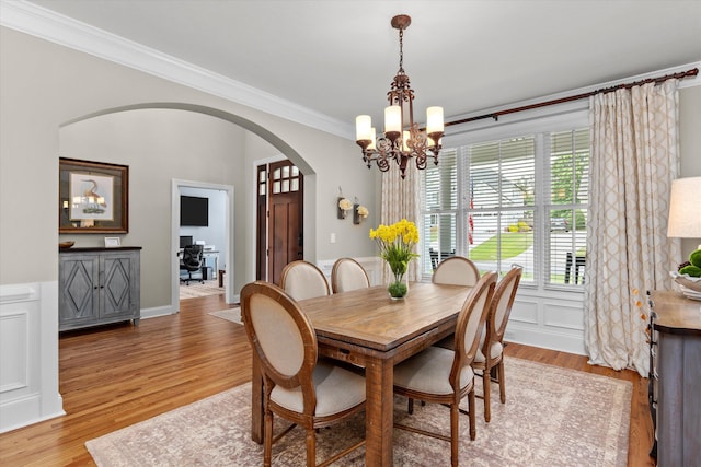 dining space featuring crown molding, arched walkways, light wood finished floors, and a chandelier