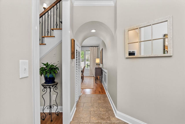 hall with baseboards, arched walkways, crown molding, and stone tile floors