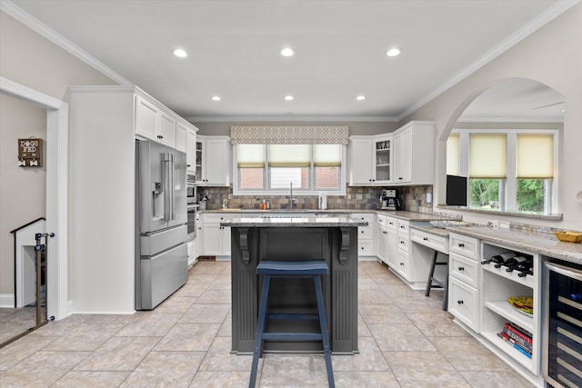 kitchen featuring arched walkways, tasteful backsplash, white cabinets, wine cooler, and stainless steel appliances