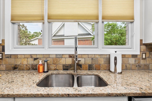 room details with white cabinetry, light stone counters, a sink, and tasteful backsplash