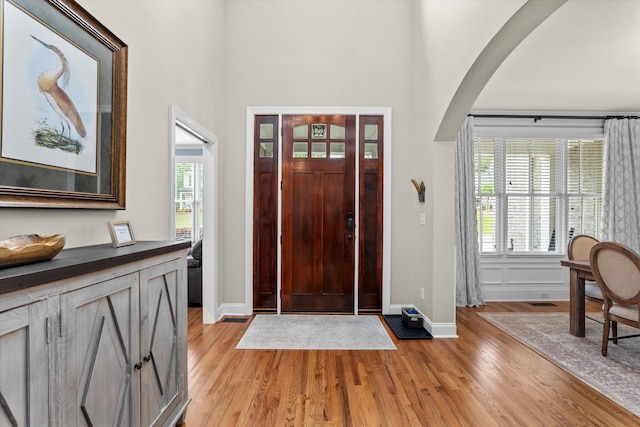 entryway featuring baseboards, arched walkways, light wood-style flooring, and a high ceiling