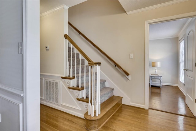 stairway featuring visible vents, ornamental molding, baseboards, and wood finished floors