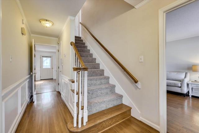 staircase featuring a decorative wall, wainscoting, crown molding, and wood finished floors