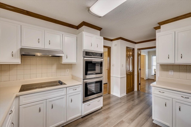 kitchen with light wood-style flooring, under cabinet range hood, white cabinetry, double oven, and black electric cooktop