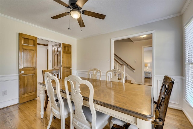 dining space with a wainscoted wall, ceiling fan, light wood-type flooring, and ornamental molding