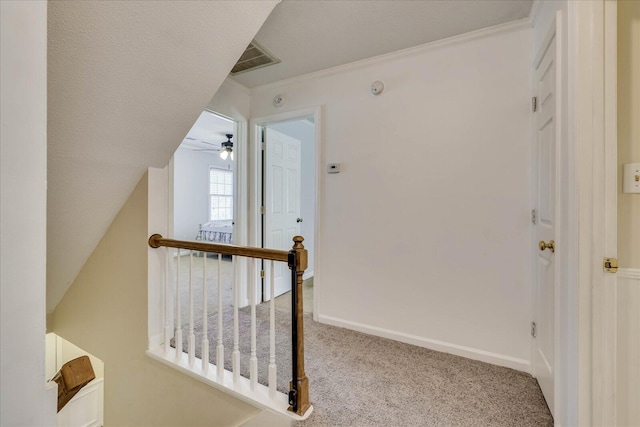 hall with visible vents, crown molding, baseboards, an upstairs landing, and carpet flooring