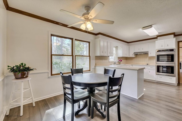 dining space featuring a ceiling fan, baseboards, light wood-style flooring, a textured ceiling, and crown molding