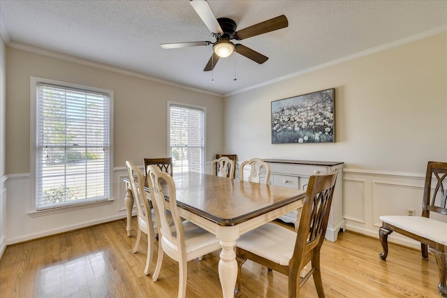 dining room with a wainscoted wall, ceiling fan, ornamental molding, a textured ceiling, and light wood-type flooring