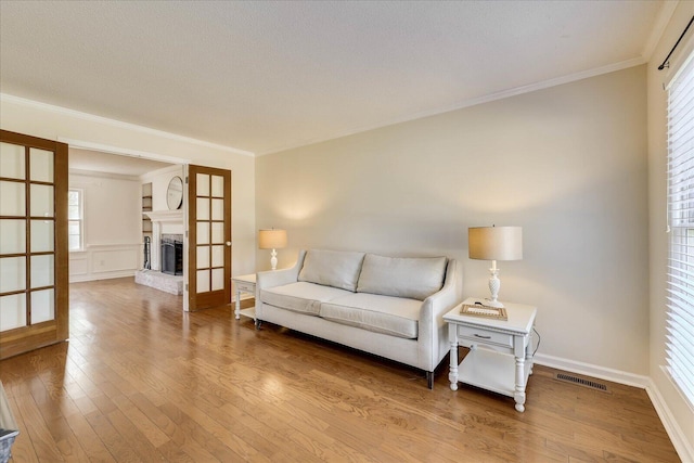 living room with visible vents, a fireplace with raised hearth, ornamental molding, wood-type flooring, and a textured ceiling