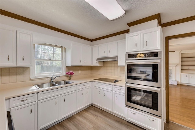 kitchen featuring light wood-style flooring, a sink, under cabinet range hood, double oven, and black electric cooktop