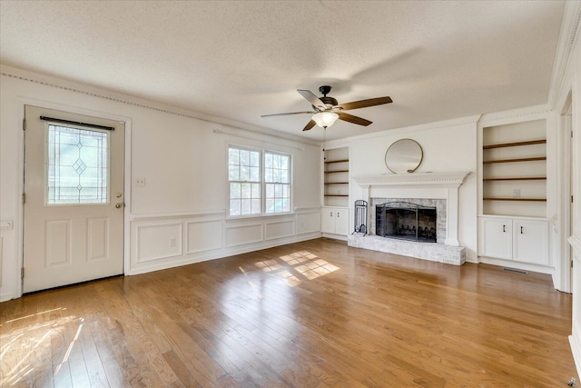 unfurnished living room featuring built in shelves, visible vents, wood-type flooring, a textured ceiling, and a brick fireplace