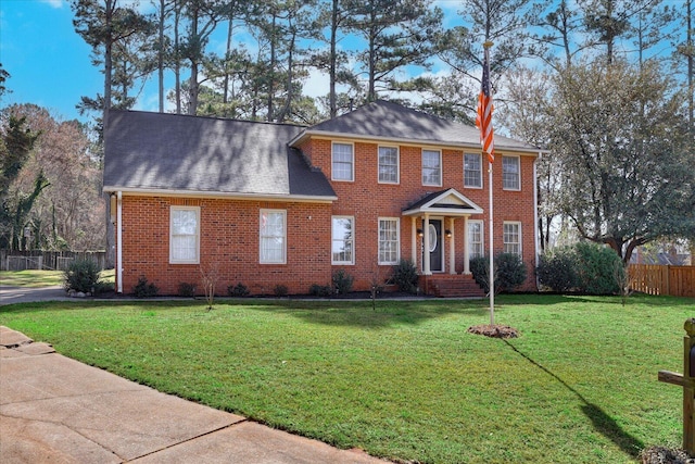 colonial-style house featuring brick siding, a front yard, and fence