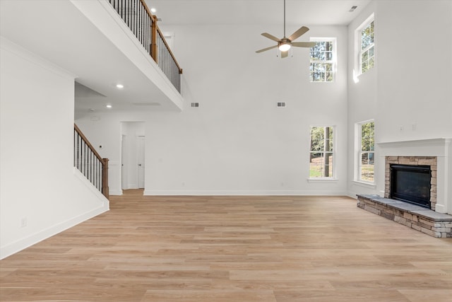 unfurnished living room featuring ceiling fan, light hardwood / wood-style floors, a towering ceiling, and a wealth of natural light