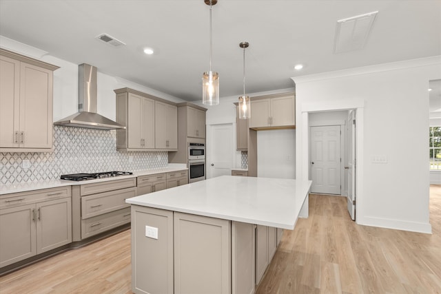 kitchen featuring decorative backsplash, appliances with stainless steel finishes, wall chimney exhaust hood, a center island, and light hardwood / wood-style floors