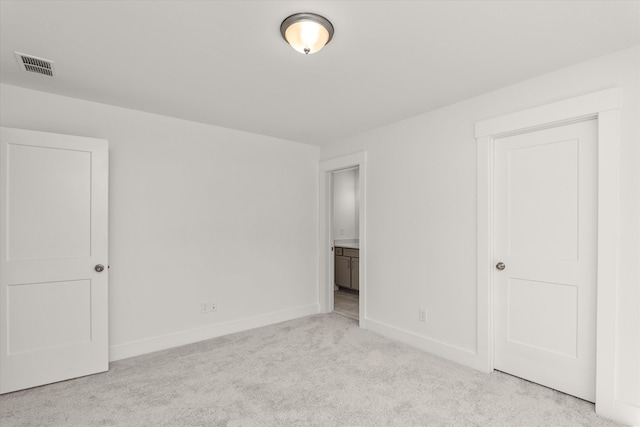 unfurnished bedroom featuring light colored carpet and ensuite bath