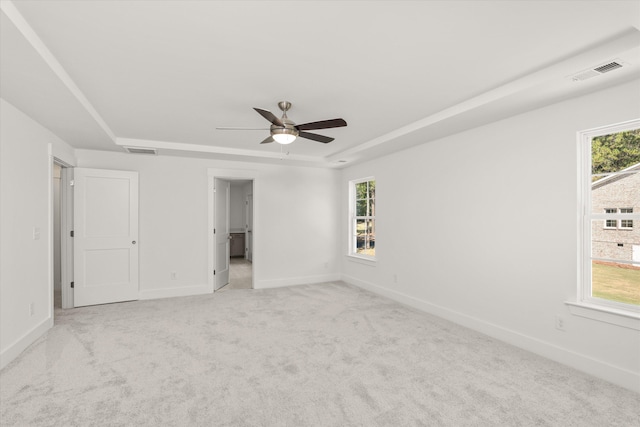 empty room featuring a tray ceiling, a wealth of natural light, ceiling fan, and light colored carpet