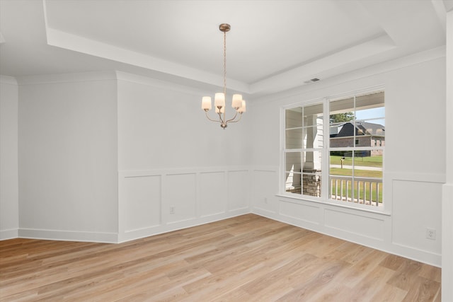 spare room with a chandelier, light wood-type flooring, and a tray ceiling