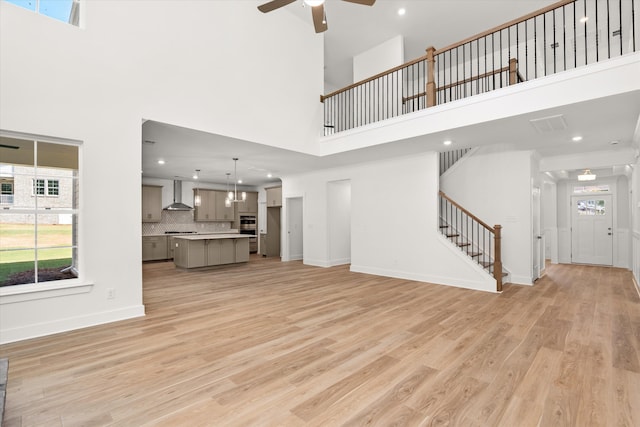 living room with a wealth of natural light, light hardwood / wood-style flooring, a towering ceiling, and ceiling fan