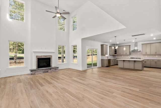 unfurnished living room with a stone fireplace, ceiling fan, light hardwood / wood-style flooring, and plenty of natural light