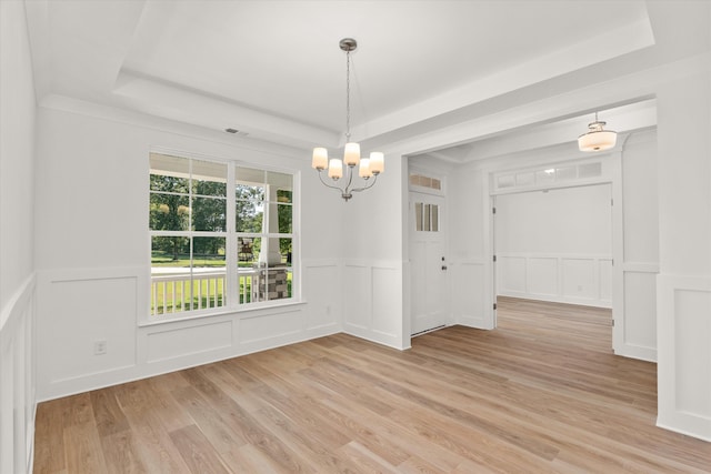 empty room featuring an inviting chandelier, a raised ceiling, and light hardwood / wood-style flooring