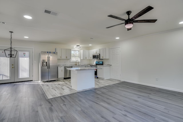 kitchen with a kitchen island, white cabinetry, stainless steel appliances, hanging light fixtures, and light hardwood / wood-style flooring