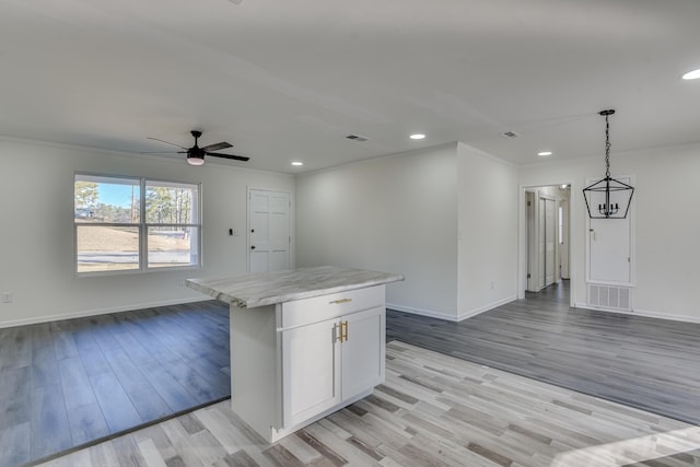 kitchen with a kitchen island, light hardwood / wood-style floors, white cabinetry, hanging light fixtures, and ceiling fan with notable chandelier