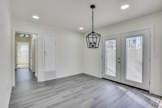 unfurnished dining area featuring light wood-type flooring, an inviting chandelier, crown molding, and french doors