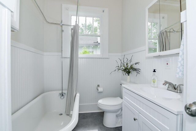 full bath featuring a washtub, plenty of natural light, wainscoting, vanity, and toilet