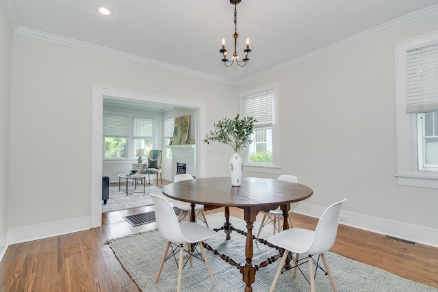 dining space featuring crown molding, wood finished floors, a fireplace, baseboards, and visible vents