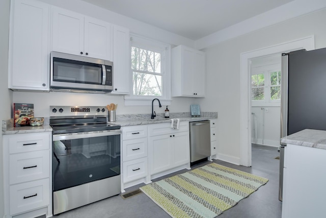 kitchen featuring a sink, white cabinetry, appliances with stainless steel finishes, light stone countertops, and visible vents