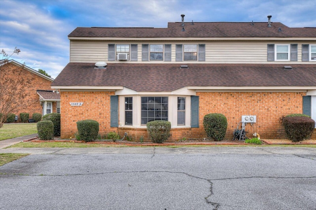 view of front of house featuring cooling unit, brick siding, and roof with shingles