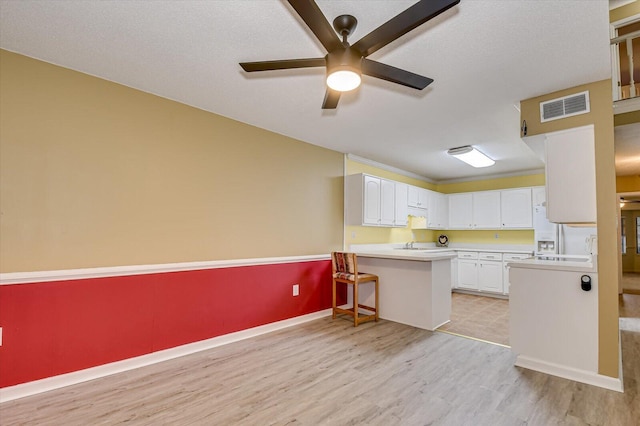 kitchen featuring visible vents, light wood-style flooring, light countertops, white fridge with ice dispenser, and white cabinetry