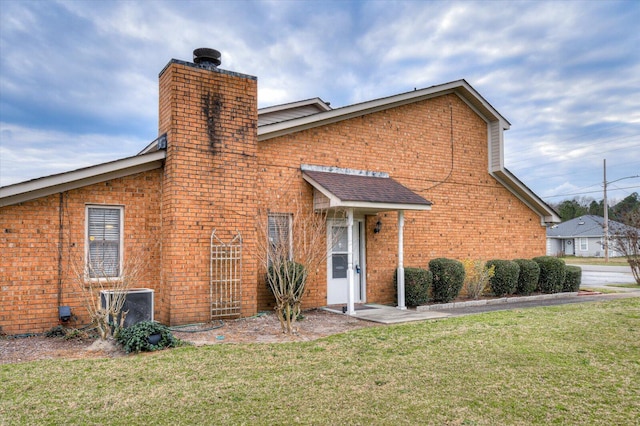 view of front facade featuring central air condition unit, brick siding, a chimney, and a front yard