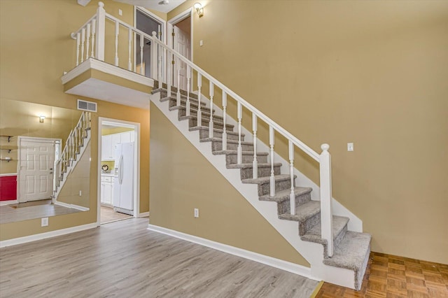 stairs with visible vents, baseboards, parquet floors, and a towering ceiling