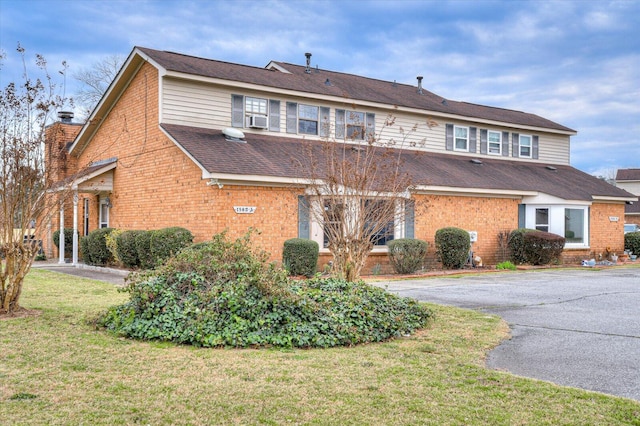 view of front facade with a front yard, cooling unit, and brick siding