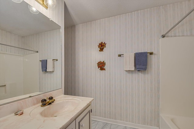 bathroom with marble finish floor, a textured ceiling, washtub / shower combination, wallpapered walls, and vanity