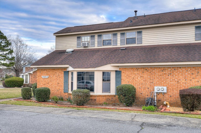 view of front facade with cooling unit, brick siding, and roof with shingles