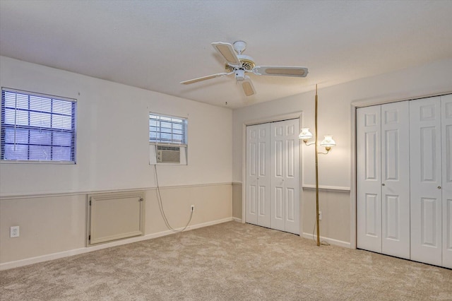 unfurnished bedroom with two closets, baseboards, light carpet, cooling unit, and a ceiling fan