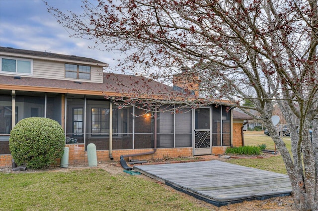 rear view of house featuring a yard, brick siding, a chimney, and a sunroom