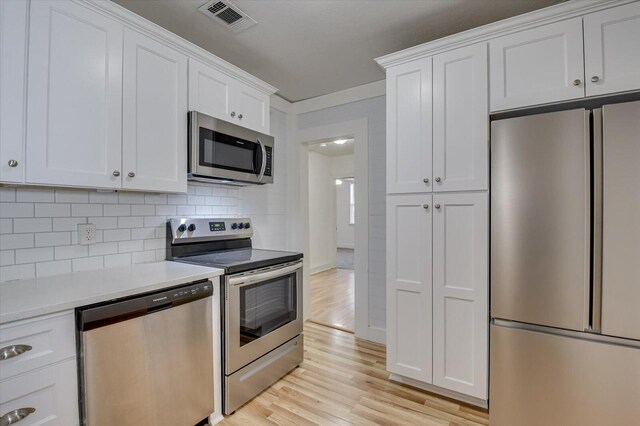 kitchen featuring white cabinets, light wood-type flooring, appliances with stainless steel finishes, and tasteful backsplash