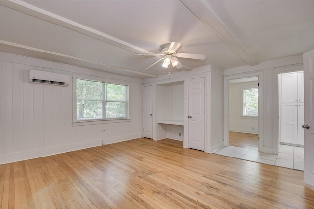 unfurnished bedroom with a wall mounted air conditioner, ceiling fan, beam ceiling, and light wood-type flooring