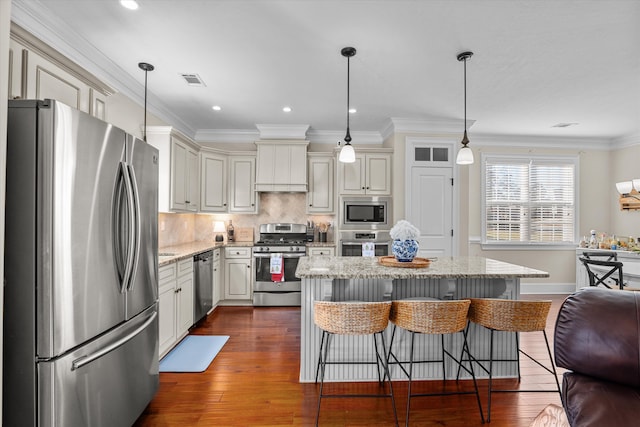 kitchen with a kitchen island, appliances with stainless steel finishes, decorative light fixtures, a breakfast bar area, and light stone counters