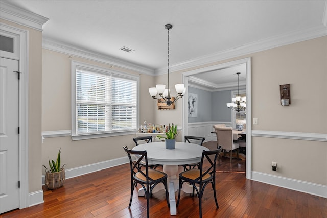 dining space with dark wood-type flooring, ornamental molding, and a chandelier