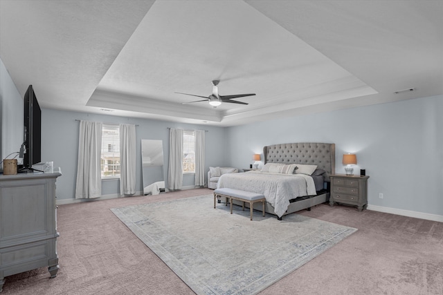 bedroom featuring ceiling fan, a tray ceiling, and light carpet