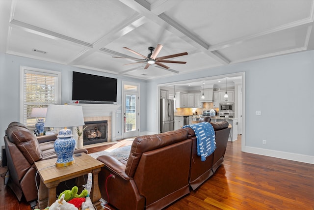 living room with beamed ceiling, dark hardwood / wood-style flooring, a tiled fireplace, coffered ceiling, and ceiling fan