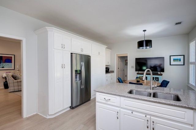 kitchen with stainless steel refrigerator with ice dispenser, a sink, light wood-style flooring, white cabinetry, and light stone countertops