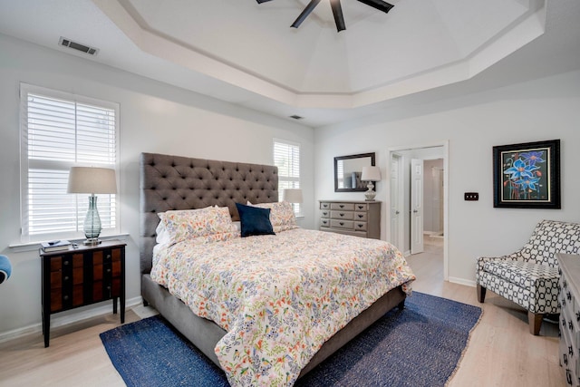 bedroom with light wood finished floors, a tray ceiling, baseboards, and ceiling fan