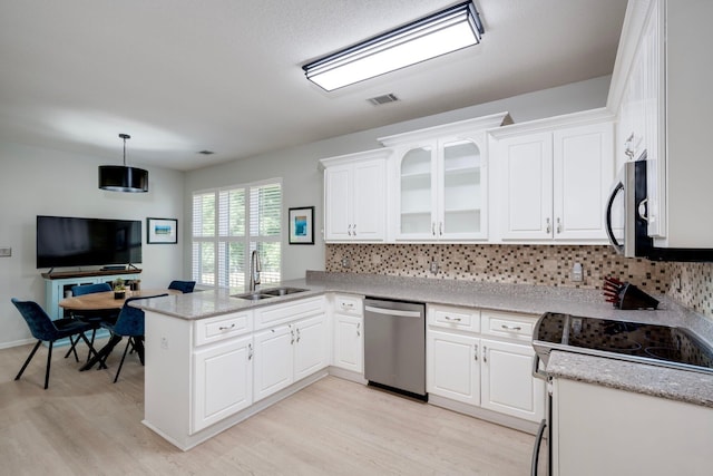 kitchen with appliances with stainless steel finishes, a sink, a peninsula, light wood finished floors, and backsplash