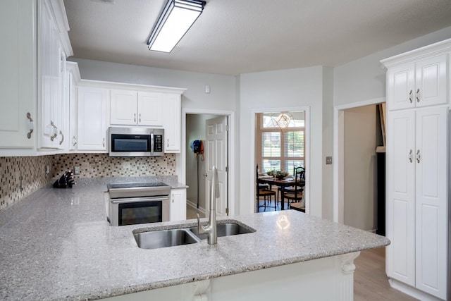 kitchen featuring appliances with stainless steel finishes, a sink, light stone countertops, white cabinets, and a peninsula