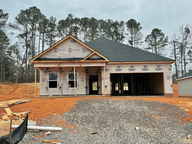 property under construction with an attached garage, roof with shingles, a porch, and gravel driveway